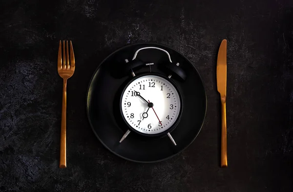 Ceas deșteptător pe o placă neagră cu cuțit de cupru și furculiță . — Fotografie, imagine de stoc