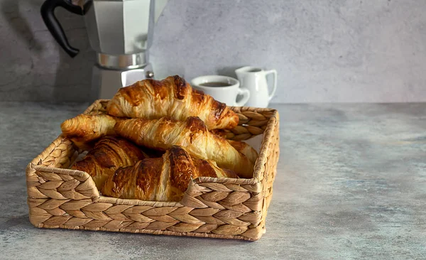 Uma cesta de vime cheia de croissants de manteiga fresca e café . — Fotografia de Stock