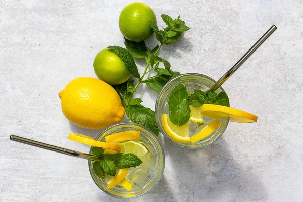 집에서 기분을 상쾌하게 해 주는 여름 레모네이드를 레몬, 라임 조각, 박하, 얼음으로 만든 음료와 함께 마시는 모습 — 스톡 사진