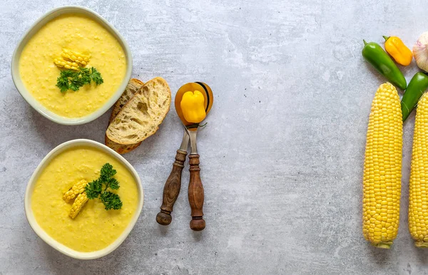 Plates with autumn spicy corn soup and ingredients. Served with corn cobs, greens, bread. Vegetarian recipe