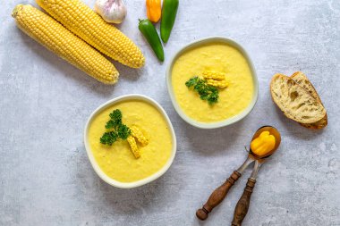 Baharatlı mısır çorbası ve malzemelerle dolu iki tabak. Mısır koçanlarıyla, yeşilliklerle, ekmekle servis edilir. Vejetaryen tarifi