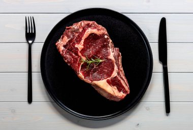 Çiğ biftekli biftek. Organik çiftlik eti. Tahta masadaki siyah tabak.