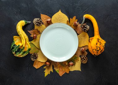 Sonbahar ve Şükran Günü sofrası. Düşen yapraklar, dekoratif balkabakları, arka planda boş beyaz tabak.