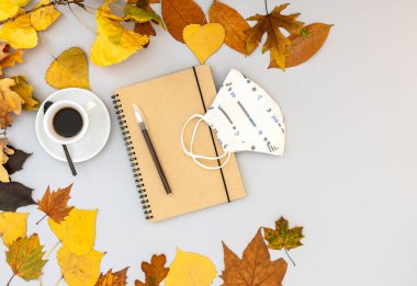 Çalışma odası, defter, maske, kalem, sonbahar yaprakları ve kahve fincanı. Düz yerde, en üst masa. Yeni normallik