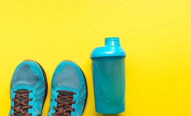 Düz spor ayakkabılar ve sarı arka planda bir şişe su. Sağlıklı bir yaşam tarzı ve konsept.