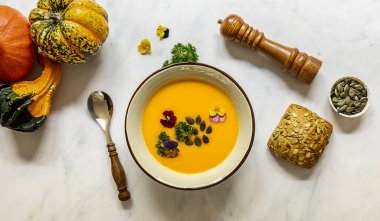 Yenilebilir çiçekler, tohumlar ve taze pişmiş ekmekle balkabağı kremalı çorba. Sağlıklı vejetaryen güz yemeği.