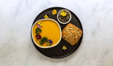 Yenilebilir çiçekler, tohumlar ve taze pişmiş ekmekle balkabağı kremalı çorba. Sağlıklı vejetaryen güz yemeği.