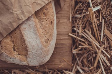 Tahtadaki buğday ekmeğine karşı altın buğday samanı. Doğal zemin. Ekmek, kağıt ve ahşap tahta üzerinde. Taze pişmiş buğday ekmeği. 