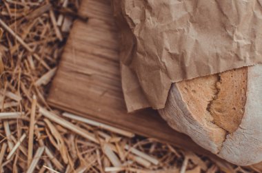 Tahtadaki buğday ekmeğine karşı altın buğday samanı. Doğal zemin. Ekmek, kağıt ve ahşap tahta üzerinde. Taze pişmiş buğday ekmeği. 