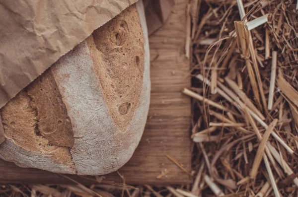 Tahtadaki buğday ekmeğine karşı altın buğday samanı. Doğal zemin. Ekmek, kağıt ve ahşap tahta üzerinde. Taze pişmiş buğday ekmeği. 