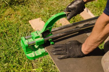 Siyah eldivenli erkek, duvar kiremitlerini kesmek için fayans kesicisini kullanıyor..