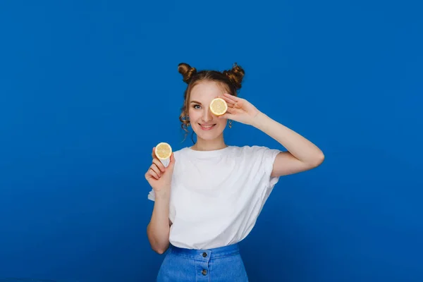 青い背景に立っている若い美少女はレモンを手に持って目を覆い — ストック写真