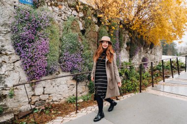 Ceketli ve şapkalı güzel romantik bir kız Annecy 'de yürüyor. Fransa. Fransa 'da çiçek açan bitkilerin arka planında şapkalı bir kız.