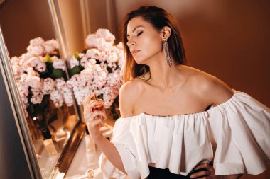 Parfümlü bir gece elbisesi giymiş genç bir kadın, giyinme masasının önünde duruyor. Kız partiye gitmeden önce parfüm kullanıyor.