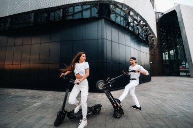 Bir kız ve bir adam şehirde elektrikli scooterlarla dolaşıyorlar. Birbirine aşık bir çift scooterlı.