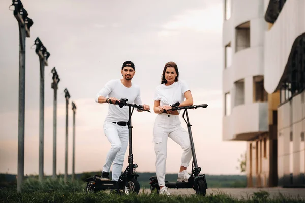 A girl and a guy are walking on electric scooters around the city, a couple in love on scooters