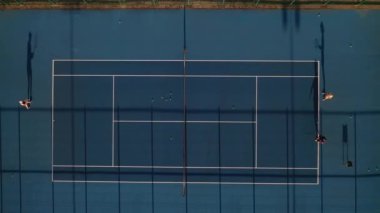 Mavi tenis kortunun en üst görüntüsü. Oyuncular antrenmanda. Akşam vakti sokakta insanlarla tenis kortu.