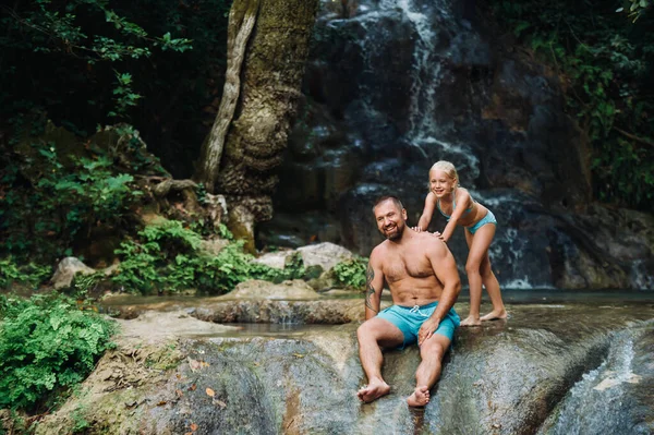 Padre con hija cerca de una cascada. Viajando por la naturaleza cerca de una hermosa cascada, el hombre y una niña de pie y disfrutar de la vista de la cascada . — Foto de Stock