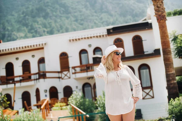 Een mooi meisje in een tuniek en hoed staat vlakbij een villa met een prachtig uitzicht.Een vrouw geniet van een vakantie in een Turks resort — Stockfoto