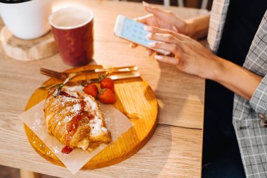 Bir kız masada oturuyor ve bir kafede akıllı telefonuyla mesajlaşıyor. Bir kız elinde telefonuyla bir kafede oturuyor. Telefona yazıyor..