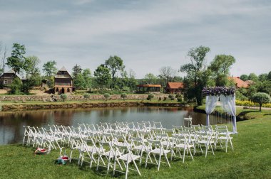 Düğün töreninin dekorasyonu yaz mevsiminde yeşil çimlerin üzerinde gölün yanında. Çok güzel dekore edilmiş bir düğün töreni..