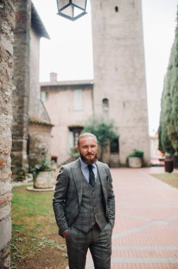 Katı gri takım elbiseli, sakallı bir adam Sirmione 'nin eski kasabasında kravat takıyor. İtalya' da gri takım elbiseli şık bir adam..