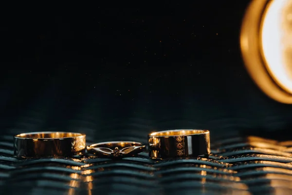 两个结婚戒指和一个订婚戒指在一个格子格子里一对恋人在灰色背景下的三枚金戒指 爱情的概念 — 图库照片