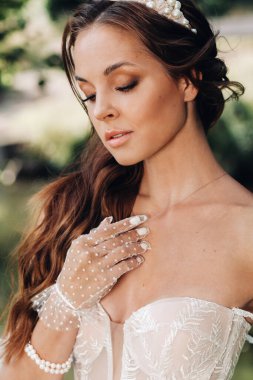 Beyaz elbiseli zarif bir gelin, parktaki şelalede çiçekli eldivenler, doğanın tadını çıkarıyor. Ormanda gelinlik ve eldiven giymiş bir model..