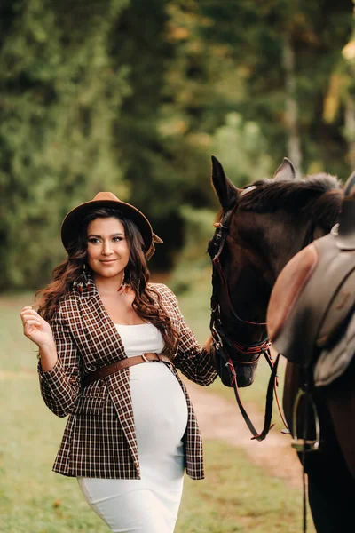 自然の中で馬の隣に大きな腹を持つ妊娠中の女の子 白いドレスと馬と茶色のジャケットのスタイリッシュな妊婦 — ストック写真