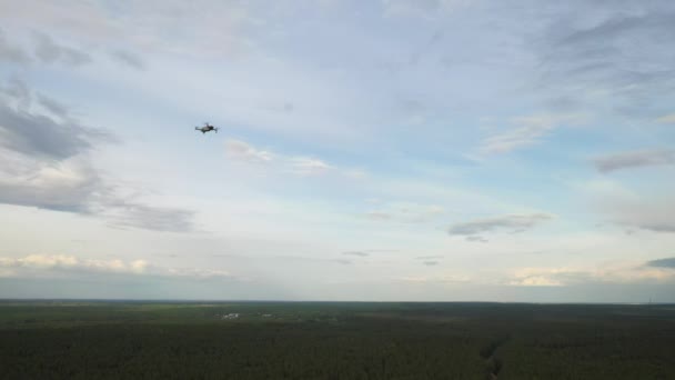 Een zwevende drone vliegt omhoog tegen de achtergrond van een bewolkte lucht en bos.De quadcopter vliegt naar het bos — Stockvideo