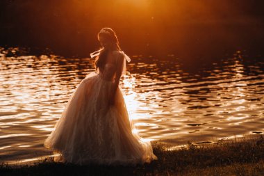 Beyaz elbiseli zarif bir gelin gün batımında doğanın tadını çıkarır. Doğada bir gelinlik içinde manken. Beyaz Rusya 'da..