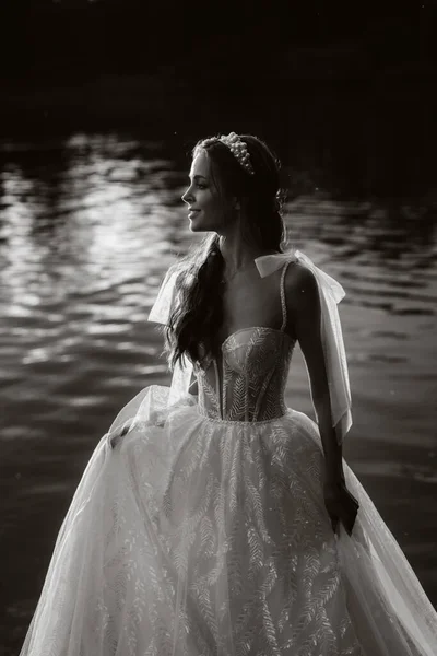 An elegant bride in a white dress enjoys nature at sunset.Model in a wedding dress in nature in the Park.Belarus.black and white photo.