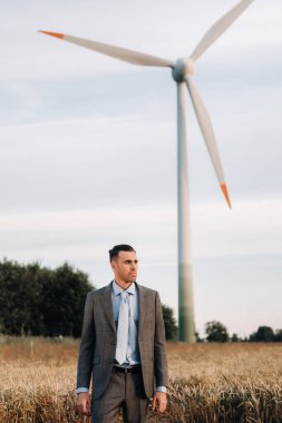 Buğday tarlasında gri takım elbiseli bir işadamının portresi bir yel değirmeninin arka planında ve akşam gökyüzünde.