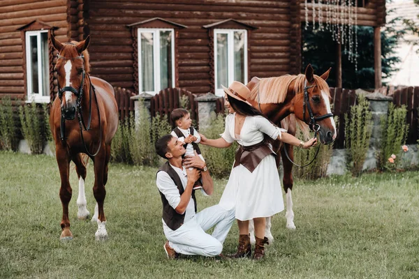 一个穿白衣的家庭和他们的儿子站在两只漂亮的马旁边 一对带着孩子的时髦夫妇和马合影 — 图库照片