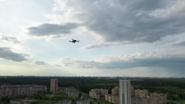 Unoszący się dron startuje na zachmurzonym niebie i tle lasu.Czworokąt leci w kierunku lasu i dzielnicy mieszkalnej miasta — Wideo stockowe