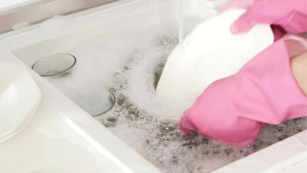 Una mujer con guantes de goma rosa lava un plato con agua del grifo en un lavabo grande en casa — Vídeo de stock