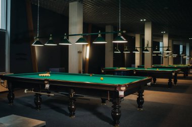 Bilardo kulübünde yeşil yüzeyi ve topları olan bir sürü bilardo masası var..