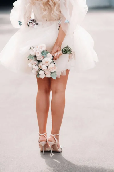 短いウェディングドレスを着た花嫁が彼女の後ろに花束を持っています — ストック写真
