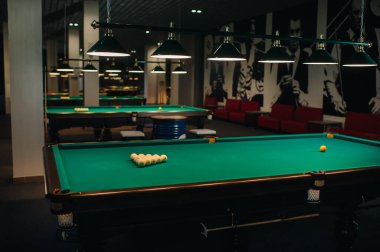Bilardo kulübünde yeşil yüzeyi ve topları olan bir sürü bilardo masası var..