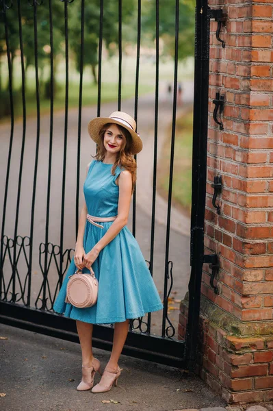 Fashionable girl in a blue dress and elegant hat on the street.