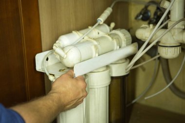 Usta, ev suyu arıtma sistemindeki kirli filtreleri değiştiriyor. İnsan eli, filtre, zar.