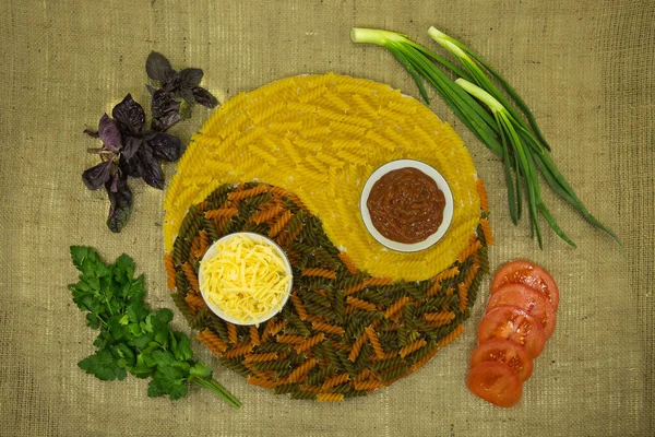 The concept of yin yang. Sign yin yang against the background of burlap. Colored pasta with natural dyes, green onion, tomatoes, parsley were used.