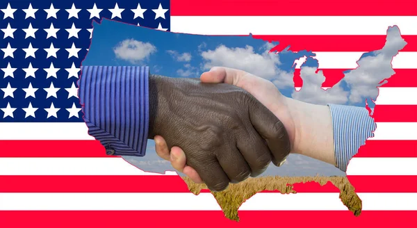 アフリカ系アメリカ人とヨーロッパ人の握手の写真を閉じます アメリカ国旗の前で握手 旗の上には米国の工場と小麦畑の輪郭があります — ストック写真