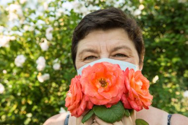 Orta yaşlı bir kadının fotoğrafı. Koronavirüsten korunmak da güzel olabilir. Bir kadın tıbbi maskeyi güllerle süsledi..