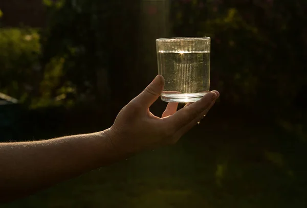 Sometimes a glass of water saves lives. A glass of water in the human hand in the sunset. Life during a pandemic.