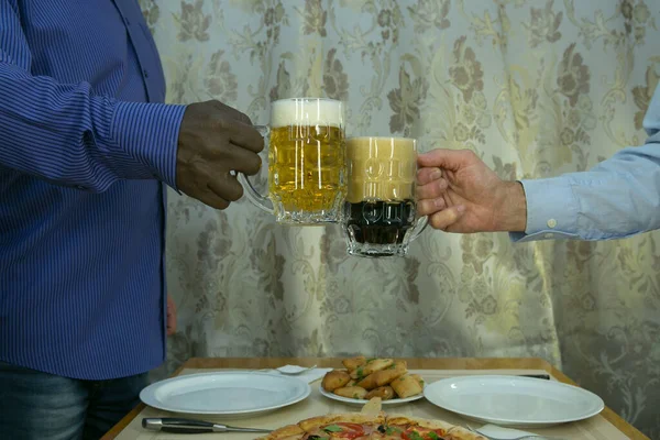 BLM. Meeting at the cafe. White and afroamerican hands are holding beer mugs with light and dark beer.