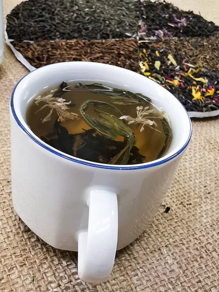 健康的なライフスタイルのコンセプト 花の混合物の追加と緑と黒のお茶のミックス 紅茶はカップで醸造される バラップの背景の写真 — ストック写真