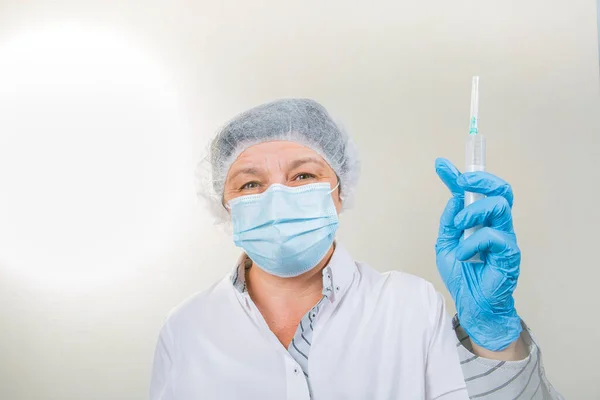 Surgical Nurse in cap and mask in medical clinic. A syringe with medicine is in the hands of a nurse. Close-up portrait. Health care, surgery.