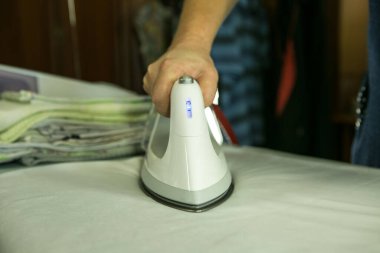 Ev ödevi. Yakın plan, çamaşırları ütüledikten sonra ütü masasında ütüleyen kadın. Buhar jeti fotoğrafta açıkça görülüyor..