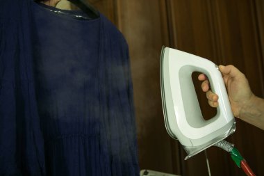 Ev ödevi. Yakın plan, çamaşırları ütüledikten sonra ütü masasında ütüleyen kadın. Elbiseyi buharlaştırma süreci. Buhar jeti fotoğrafta açıkça görülüyor..